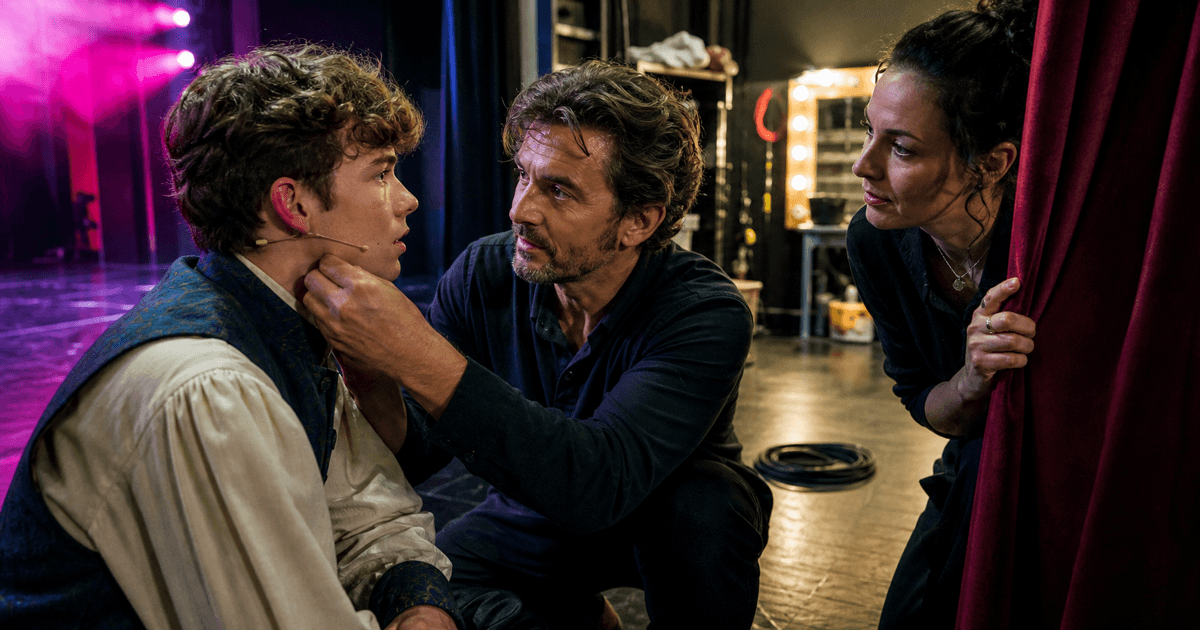 A backstage coordinator calmly fits a microphone for a nervous performer before a community theatre show